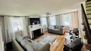 A living room with a fireplace, a sofa, a TV, and a dining area with a table and chairs. - ANY BIG PARTY!!!! (Standish)