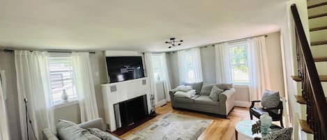 Una sala de estar con chimenea, un sofá, un televisor y un comedor con una mesa y sillas.