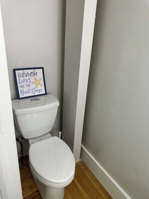 A bathroom with a white toilet, a wooden floor, and a sign on the wall that reads "BEACH DAYS ARE THE BEST DAYS" with a starfish graphic. - Family, friends, Gathering (Standish)