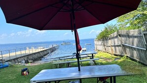 A backyard with picnic tables and a red umbrella, overlooking a body of water with boats. - ANY BIG PARTY!!!! (Standish)