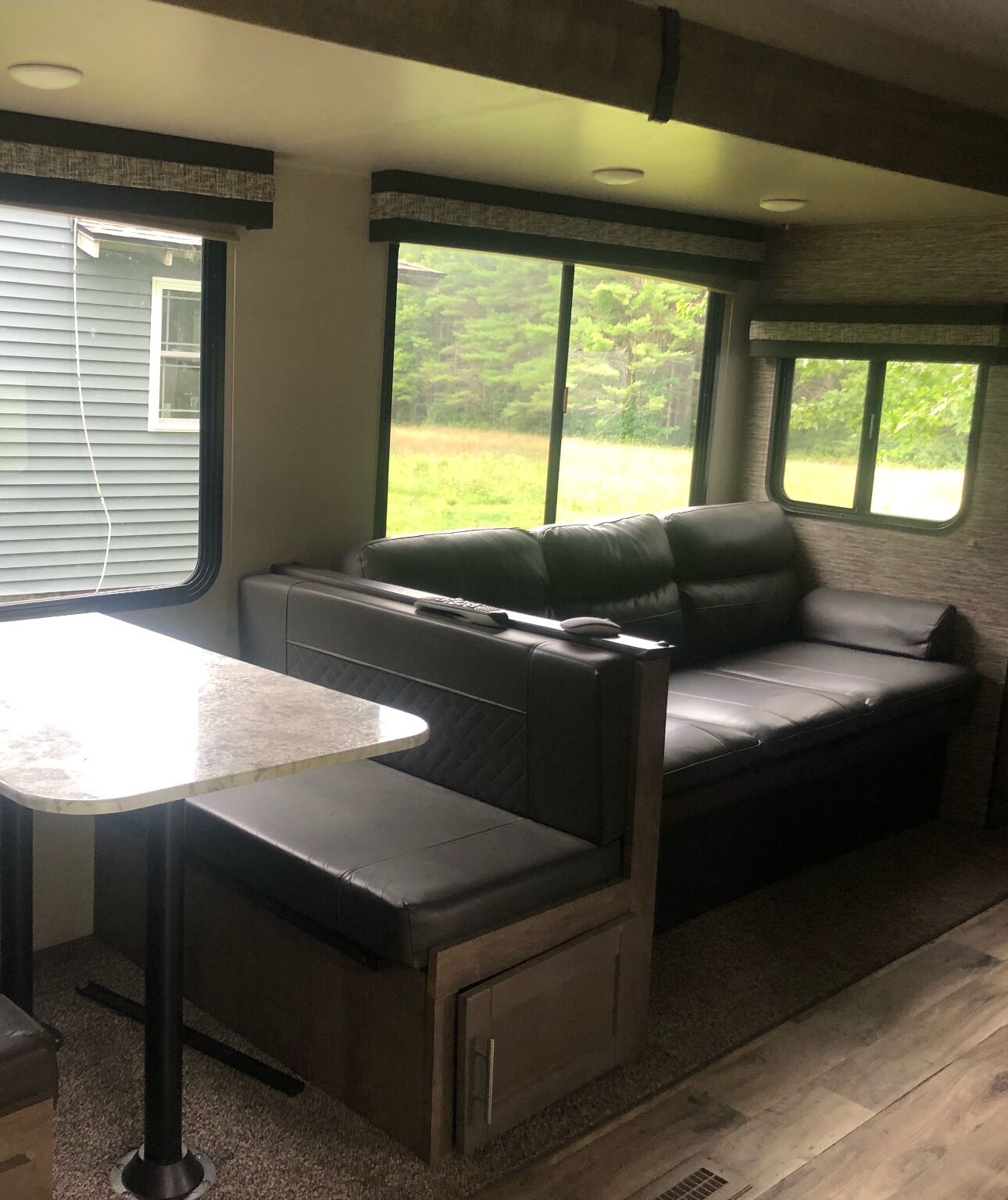 A cozy RV interior with a dining area, a seating area, and large windows offering a view of the outdoors.