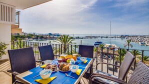 Un balcón con una mesa lista para el desayuno, con vistas a un puerto deportivo con barcos y un cielo despejado.