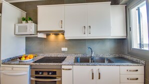 Una cocina moderna con gabinetes blancos, un lavamanos de acero inoxidable, un microondas integrado y una estufa a gas.