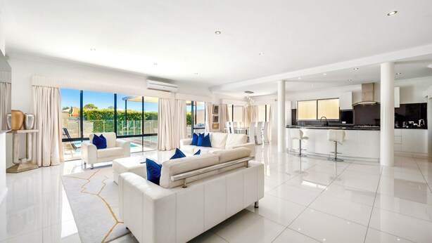 Amplia sala de estar con un sofá blanco, cojines azules y un ventanal con vistas al verdor.