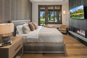 Quarto com cama, TV, lareira e janela com vista para árvores.