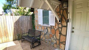 A stone exterior wall with a window, a wooden fence, a bench, and a door.