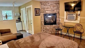 A hotel room with a bed, a fireplace, a TV, and a small kitchenette.