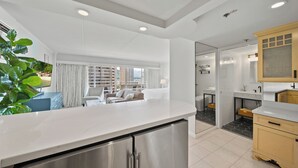 Een moderne keuken met een groot eiland, een zithoek met een bank en stoelen, en uitzicht op hoge gebouwen.