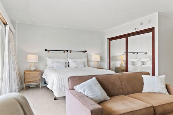 Une chambre avec un grand lit, des tables de chevet avec des lampes, un canapé marron et un miroir.