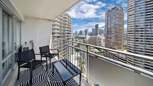 Een balkon met een tafel en stoelen, met uitzicht op een stadsgezicht met hoge gebouwen.