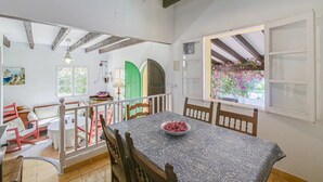 Un coin repas avec une table dressée pour quatre personnes, des chaises en bois et un saladier de fruits posé sur la table. Un escalier mène à un niveau supérieur, d’où l’on peut admirer la verdure environnante.