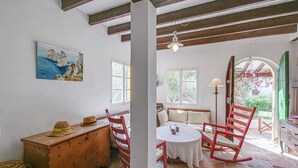 Une pièce chaleureuse avec un coffre en bois, une table ronde et des chaises rouges. Un tableau orne le mur et une fenêtre offre une vue sur la verdure.