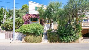 Un immeuble résidentiel à la façade blanche, aux volets verts et au petit porche orné de plantes à fleurs violettes.