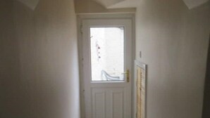 A narrow hallway with a white door at the end, leading to a room with a window. - 2 Railway Terrace (Hurworth Place)