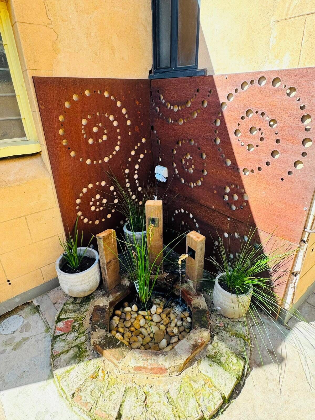 Un élément décoratif pour le jardin, composé d’un motif circulaire en pierre, de plantes en pot et d’une fontaine.