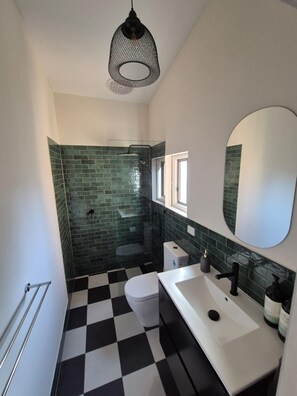A bathroom with a checkered floor, a white toilet, a white sink, a black faucet, a green-tiled shower area, and a hanging light fixture.