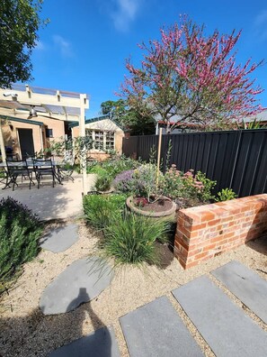 A backyard with a patio, a brick wall, and various plants.