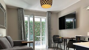 A modern room with a sofa, a dining table, chairs, a TV, and a sliding glass door leading to a balcony with greenery. - Central Studios (Cardiff)
