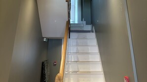 A staircase with white steps and a wooden handrail, leading to a landing with a white ceiling and recessed lighting. - Central Studios (Cardiff)
