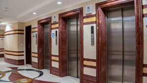 Une rangée d’ascenseurs aux parois en marbre et en bois, numérotés 101 et 102, dans un immeuble moderne.