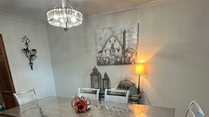 A dining room with a marble table, white chairs, a bench, a chandelier, wall art, and a rug.