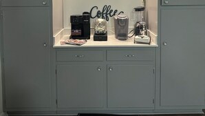 A kitchenette with a clock, coffee maker, and a coffee sign on the wall.