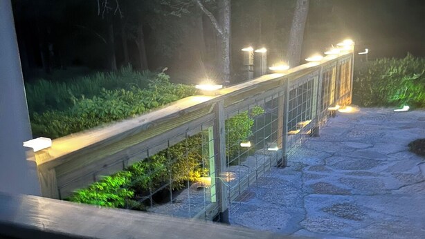 A wooden bridge with lights, surrounded by greenery and trees.