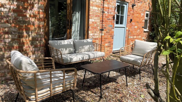 A cozy outdoor seating area with a sofa, two chairs, and a coffee table, set against a brick wall with a blue door and windows. - Cottage with beautiful garden, 7 mins from Henley-on-Thames (Binfield Heath)