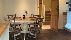 A dining area with a round table, six chairs, a vase with flowers, and a wooden door leading to a staircase. - Cottage with beautiful garden, 7 mins from Henley-on-Thames (Binfield Heath)