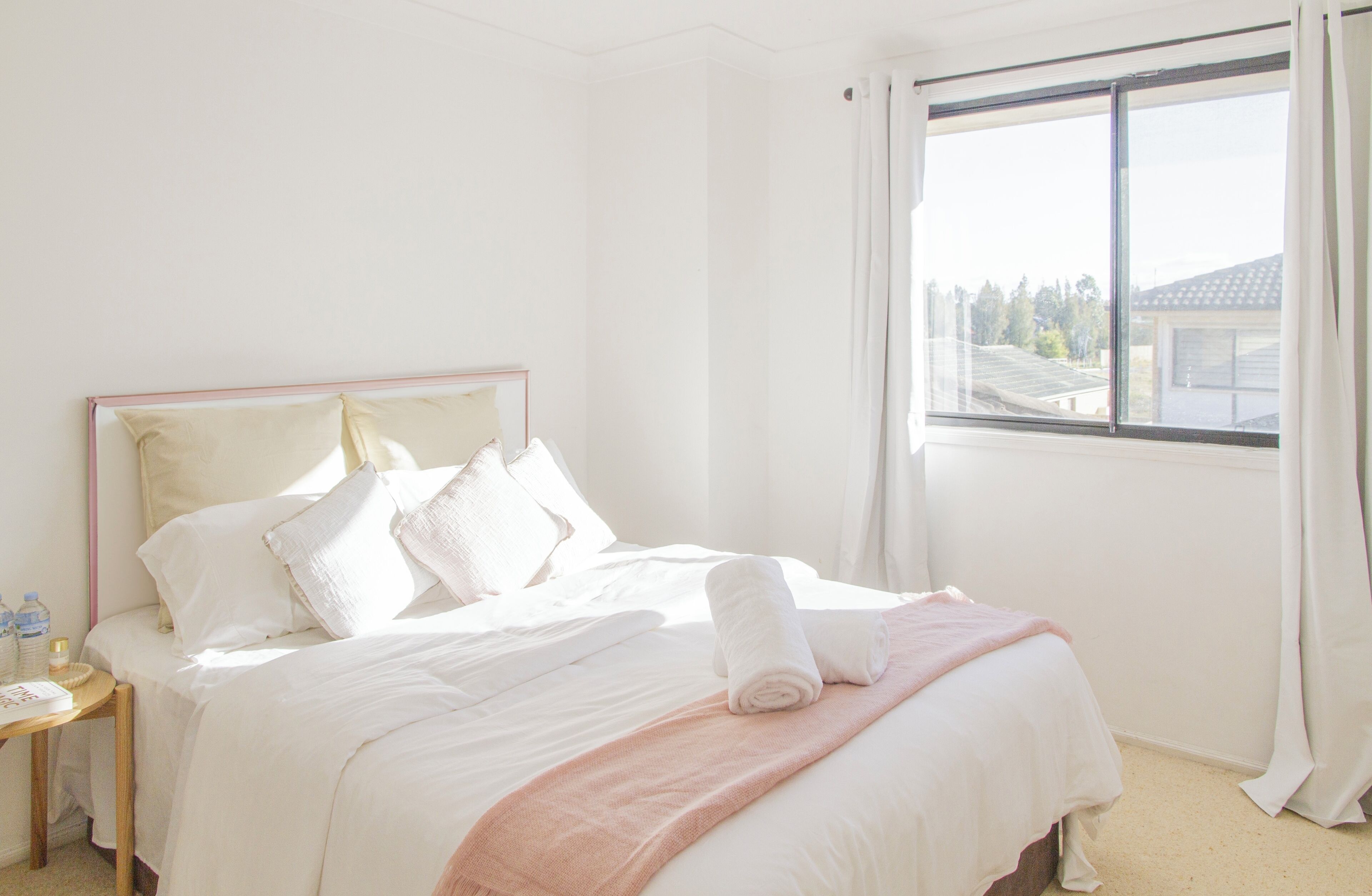 Habitación de hotel con cama, mesita de noche, ventana con cortinas y vistas a edificios.
