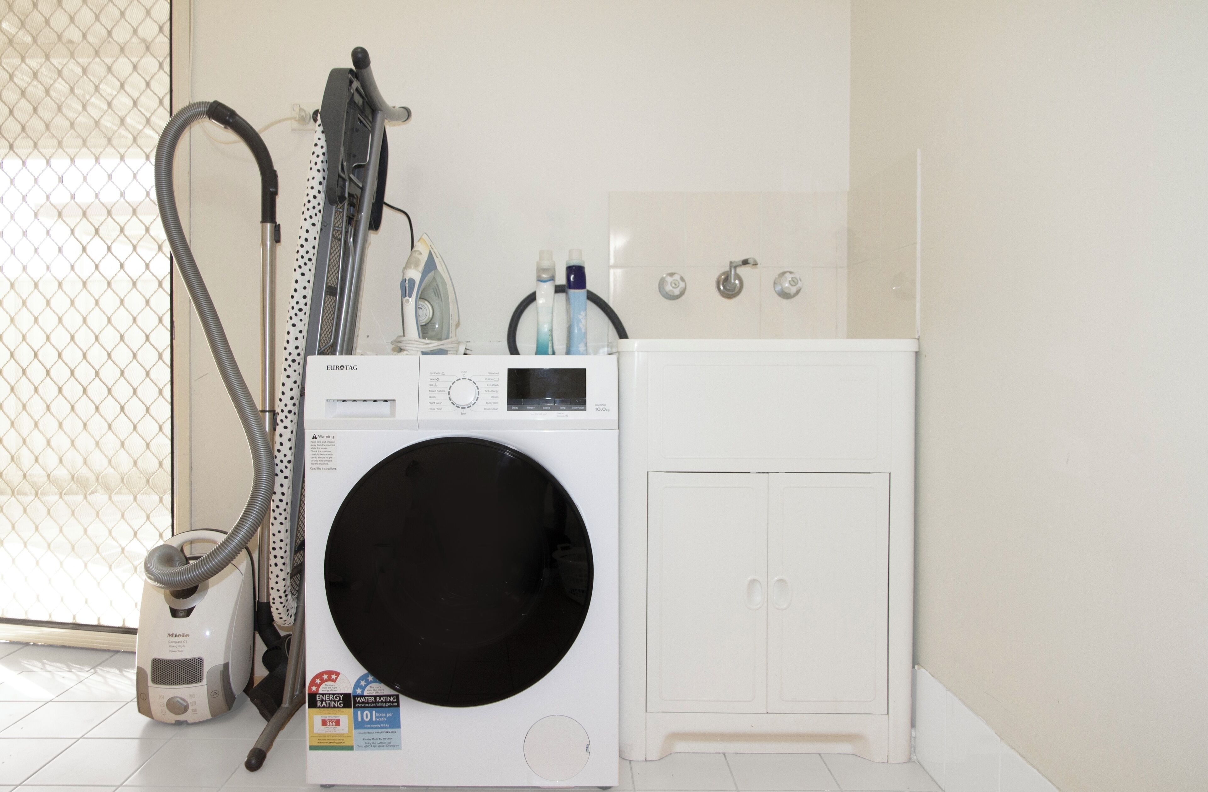 A front-loading washing machine, a vacuum cleaner, and a cabinet in a laundry room.