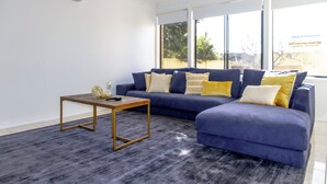 A modern living room with a blue sectional sofa, a small wooden coffee table, and a grey carpet. - Spacious, Sunlit & Recently Renovated Family Home - 4BD & Hotel Quality Bedding (Prestons)