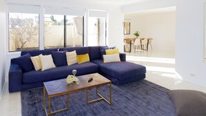 A modern living room with a sectional sofa, a coffee table, and a dining area in the background. - Spacious, Sunlit & Recently Renovated Family Home - 4BD & Hotel Quality Bedding (Prestons)