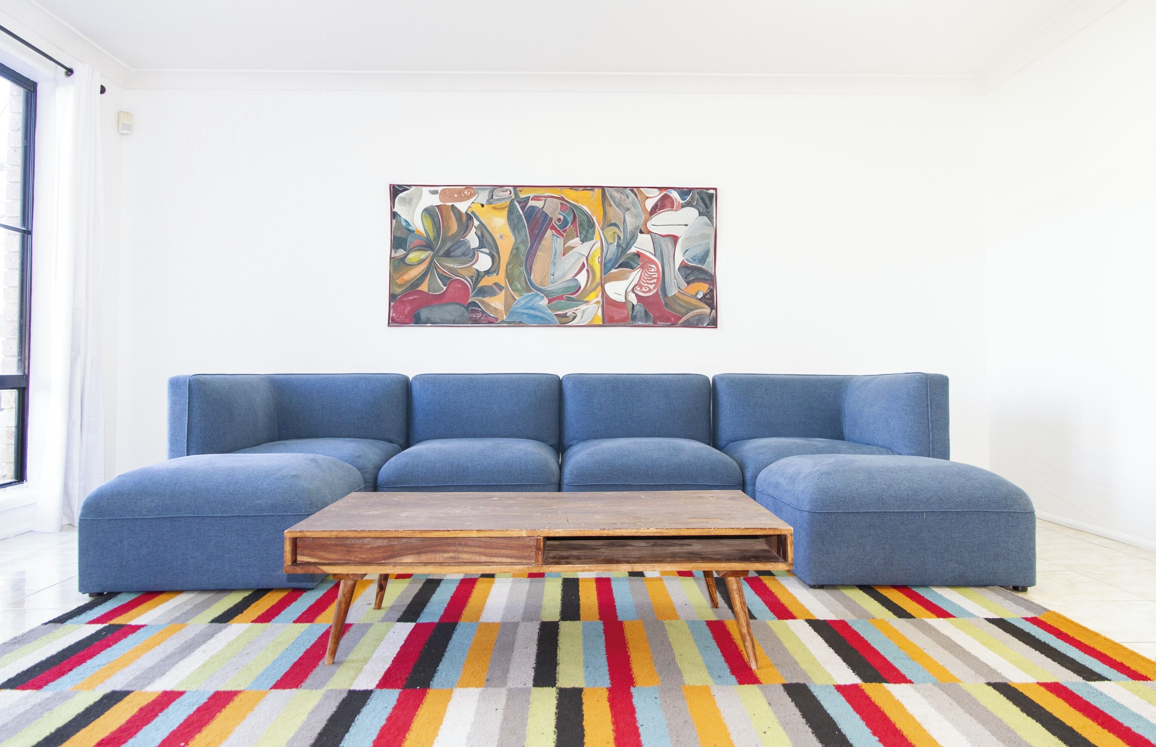 A living room with a blue sofa, a wooden coffee table, and a colorful striped rug.