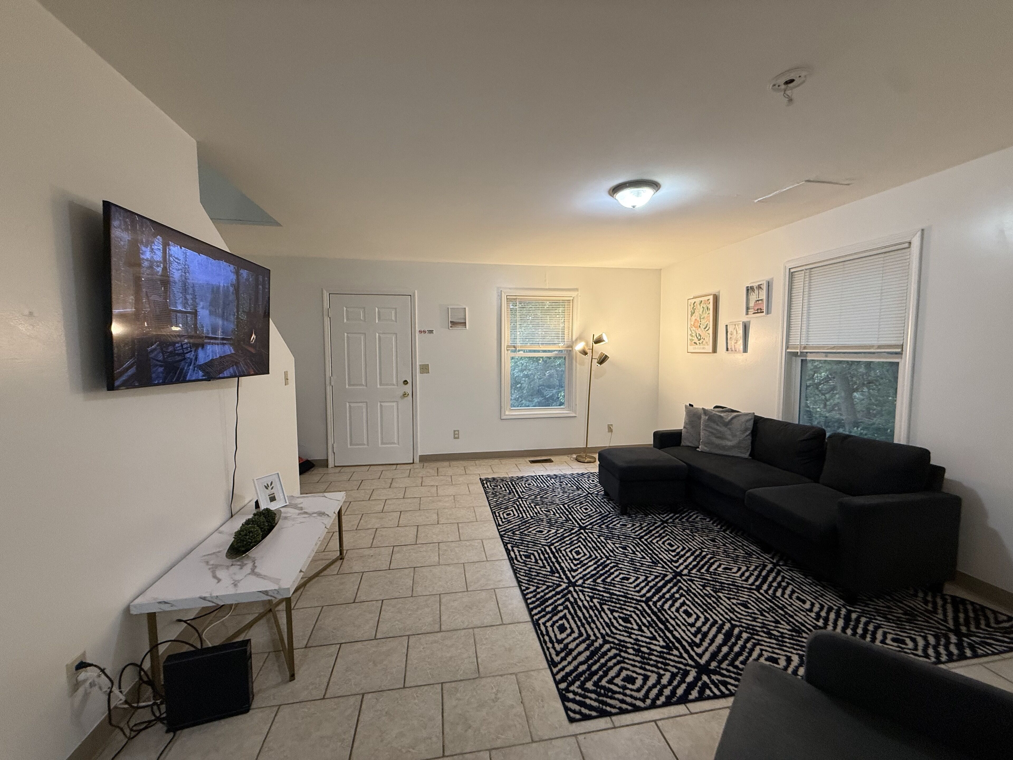A living room with a television, a sofa, a patterned rug, and a door leading to another room.