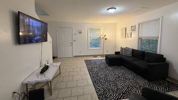 A living room with a television, a sofa, a patterned rug, and a door leading to another room.