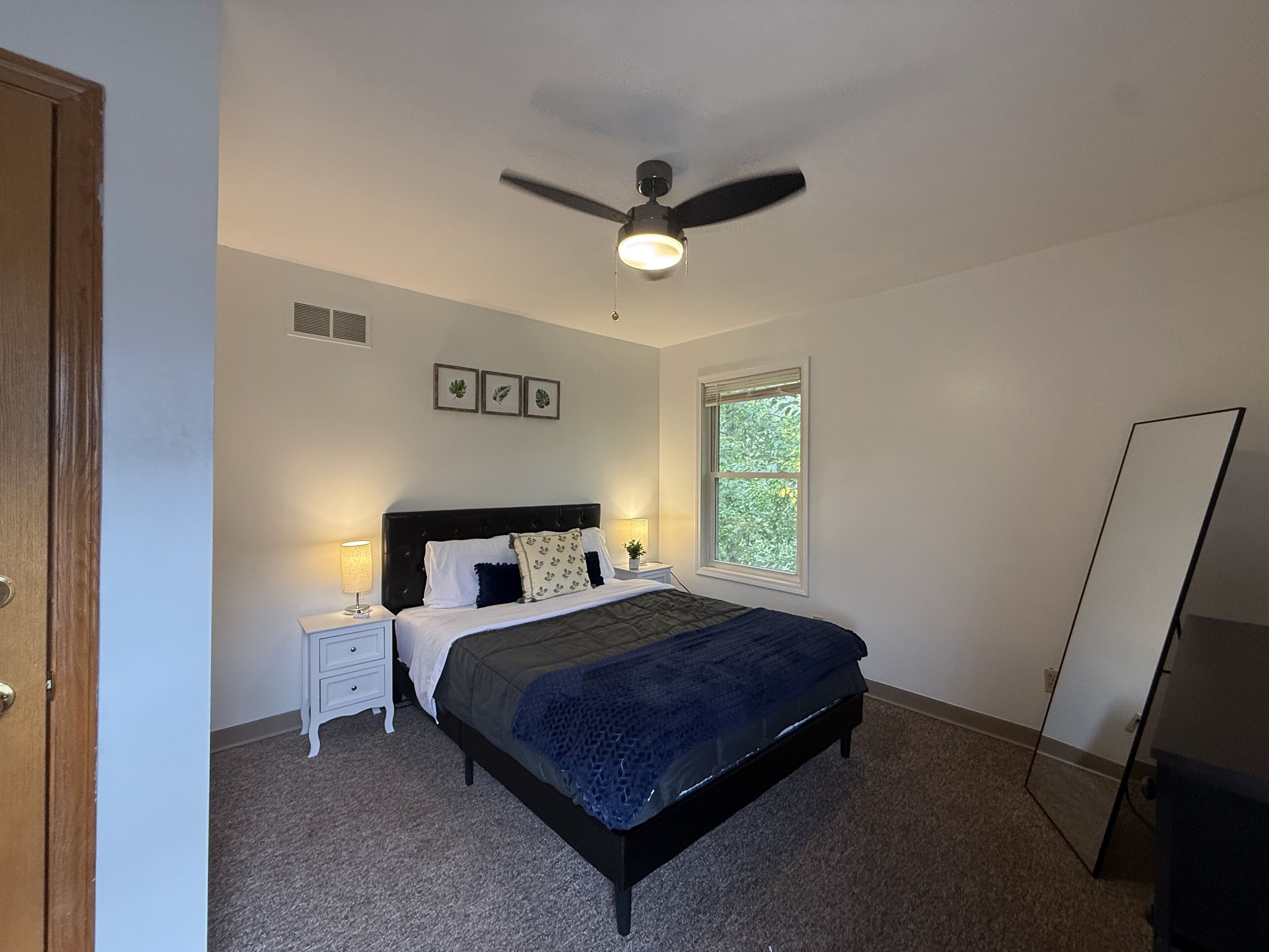 Una camera da letto con un letto, comodini, una ventola a soffitto, una finestra e uno specchio.