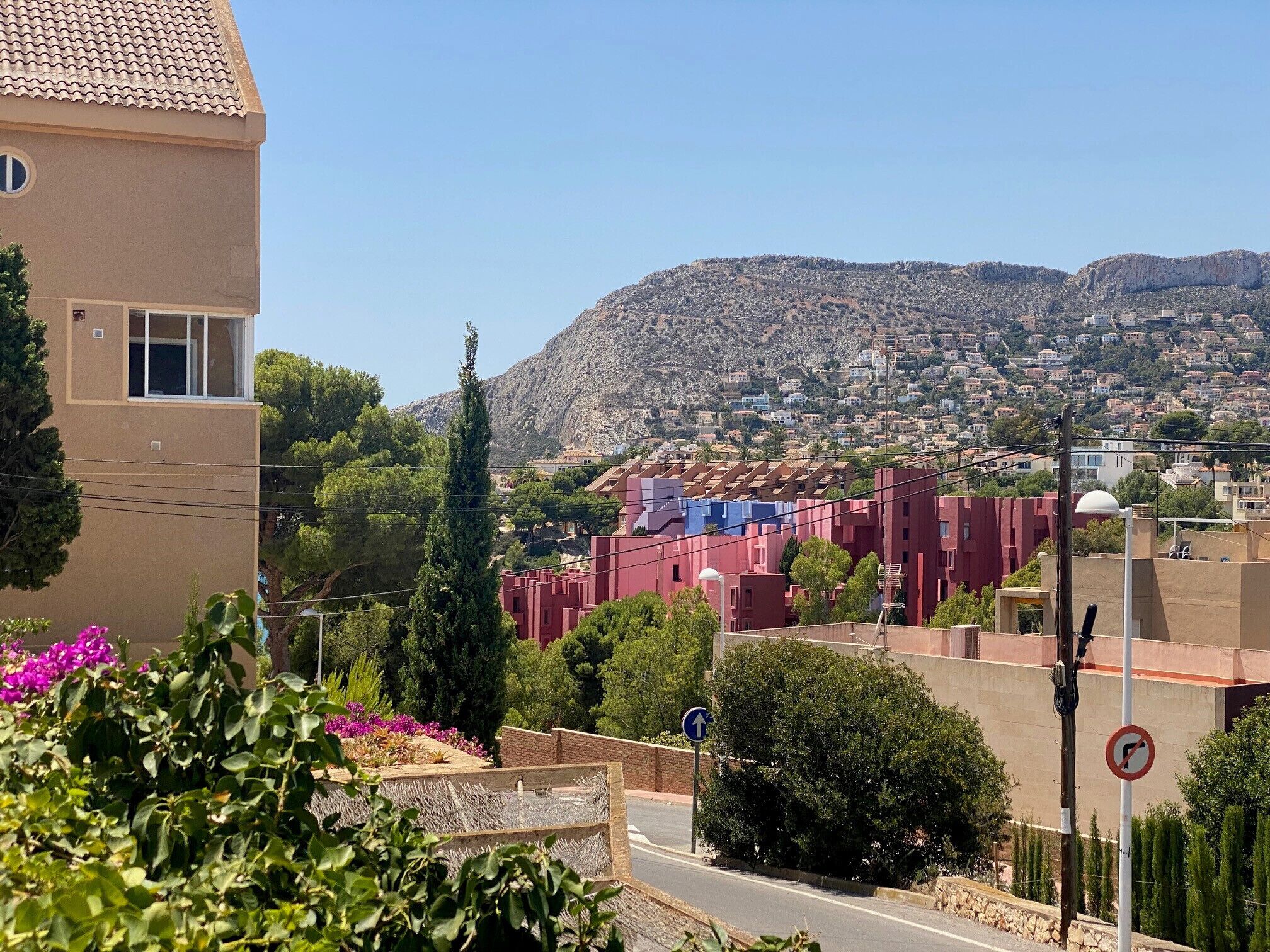 Un quartier résidentiel avec un bâtiment imposant, une rue où le stationnement est interdit, et un paysage montagneux en arrière-plan.