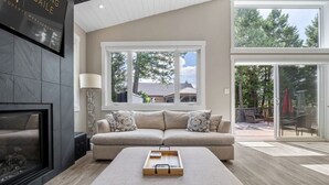 En moderne stue med pejs, sofa og stort vindue med udsigt til en terrasse.