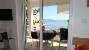 Une pièce dotée d’une porte-fenêtre coulissante donnant sur un balcon avec une table et des chaises, un téléviseur fixé au mur et un petit bureau avec un ordinateur.