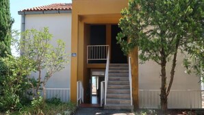 Un immeuble à la façade jaune, avec un escalier menant à un balcon et une enseigne indiquant le numéro 102.