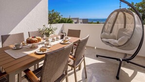 A sunlit outdoor dining area with wicker chairs, a hanging chair, and a table set with plates, cups, and a pitcher. - Villa Lea by Interhome (Crikvenica/Jadranovo)