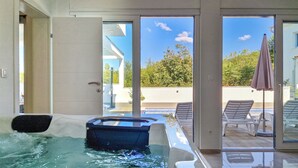 A modern indoor swimming pool with clear glass walls, a lounge area with chairs, and a view of the outdoors. - Villa Lea by Interhome (Crikvenica/Jadranovo)
