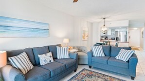 Ein modernes Wohnzimmer mit zwei Sofas, einem Deckenventilator und einer Küche im Hintergrund.