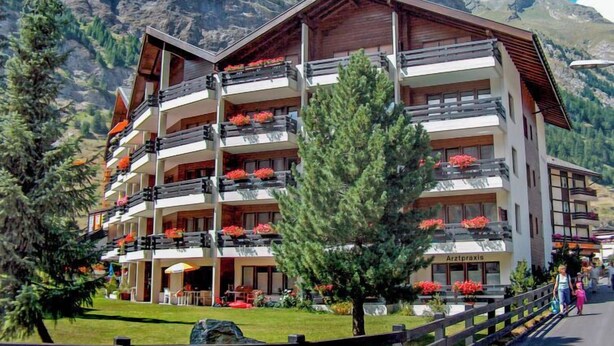 Un hôtel à plusieurs étages doté de balcons, entouré de montagnes et de verdure.