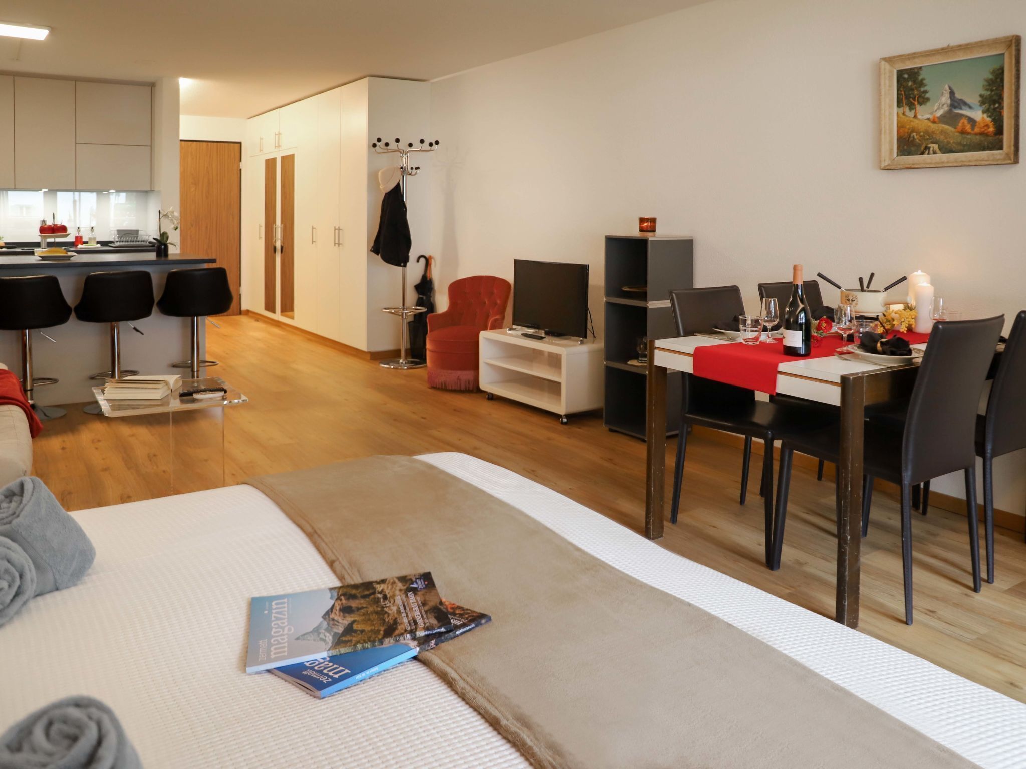 A modern hotel room with a bed, a dining area, a TV, and a coat rack.