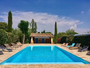 Ein rechteckiger Pool mit Liegestühlen und einem kleinen Gebäude mit einem Ziegeldach.