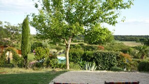 A garden with a table and chairs, a tree, and a view of a pool and landscape.