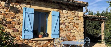 Un bâtiment en pierre avec une fenêtre et une table entourée de chaises à l’extérieur.