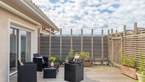 Un patio al aire libre con mobiliario de mimbre, plantas en macetas y una terraza de madera.